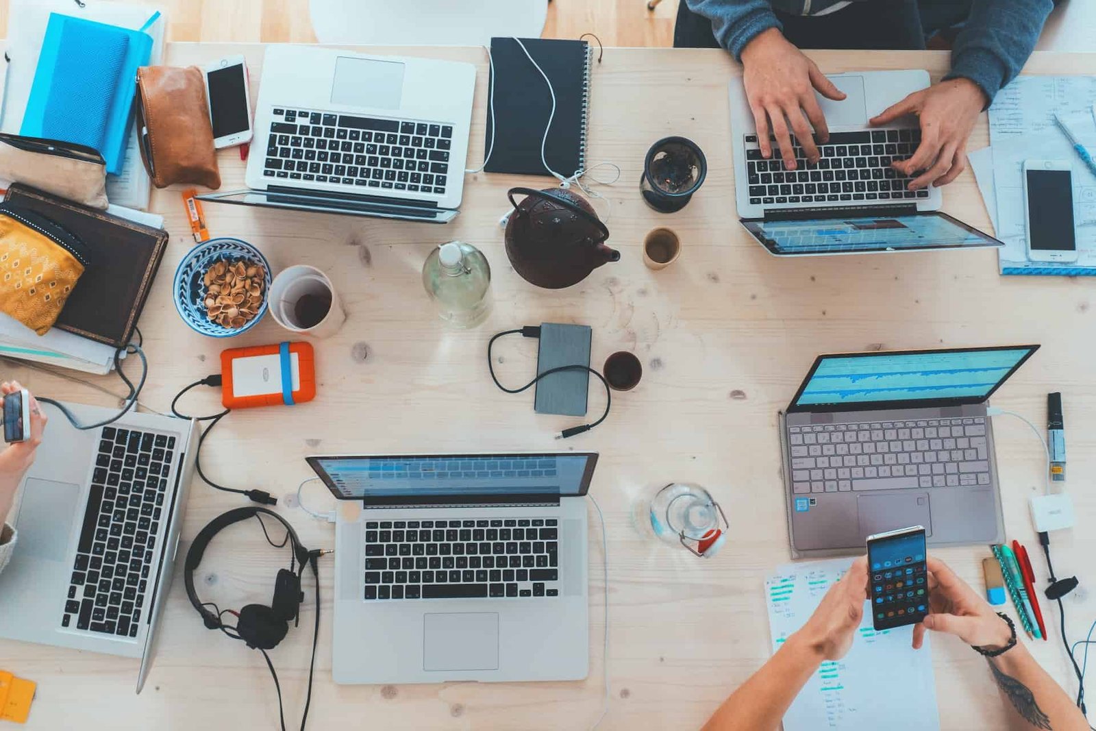 Multiple laptops and other electronics strewn across the large wooden table